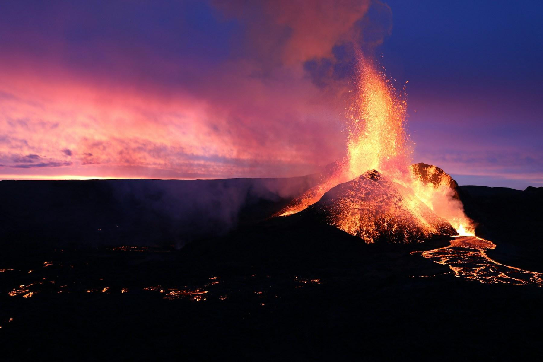 A volcano emitting glowing lava and smoke at dusk